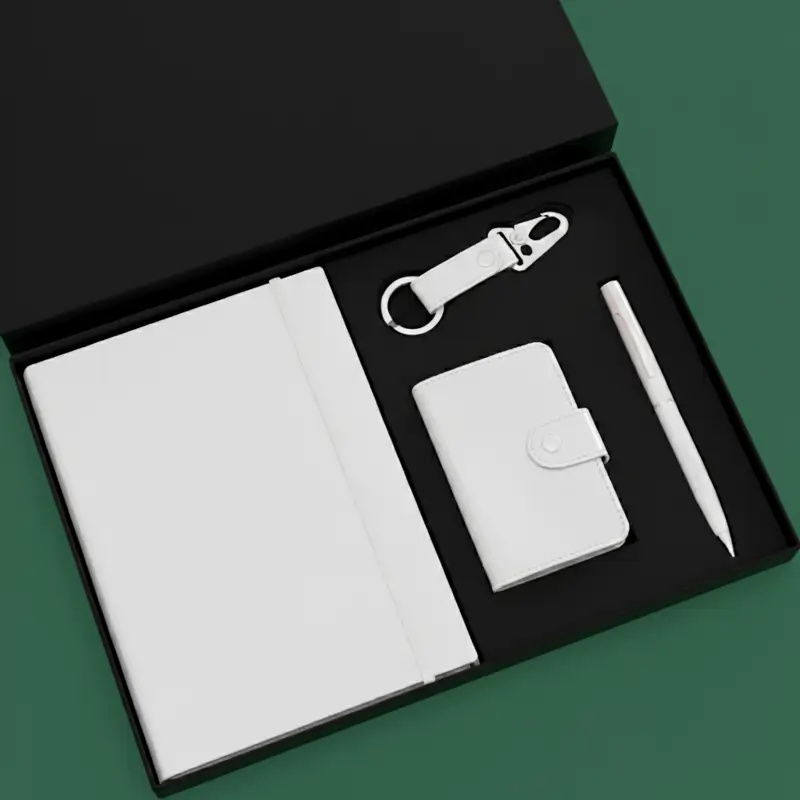A black gift box containing a white notebook, keychain, cardholder and pen, all neatly organized in a foam insert